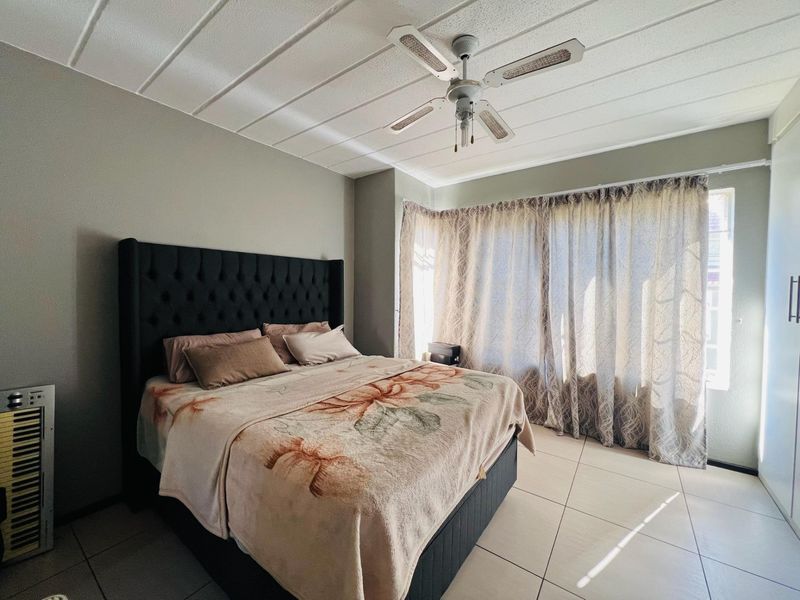 A bedroom featuring tiled flooring, a ceiling fan, and built-in wardrobe storage, with natural light entering through large windows.