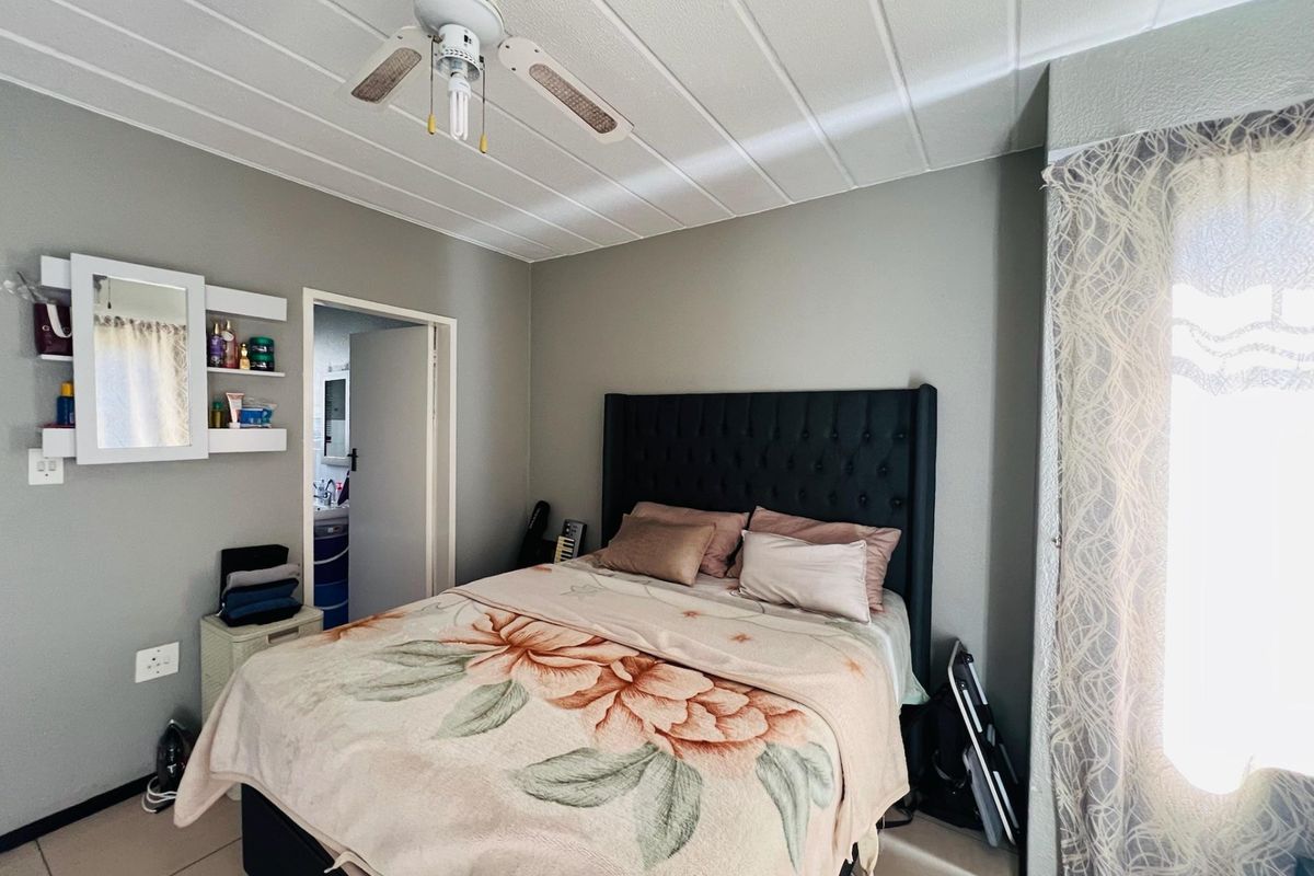 A bedroom featuring tiled flooring, a panelled ceiling, a ceiling fan, and built-in wall shelving, with an adjoining doorway leading to an en-suite bathroom.