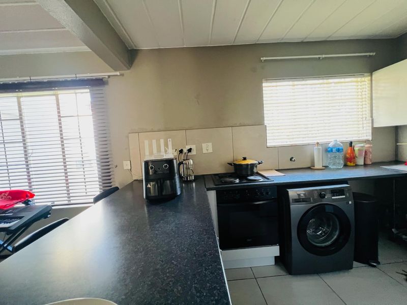 Functional kitchen area featuring dark laminate countertops, built-in oven with hob, tiled backsplash, and neutral wall finishes with natural light from window blinds.