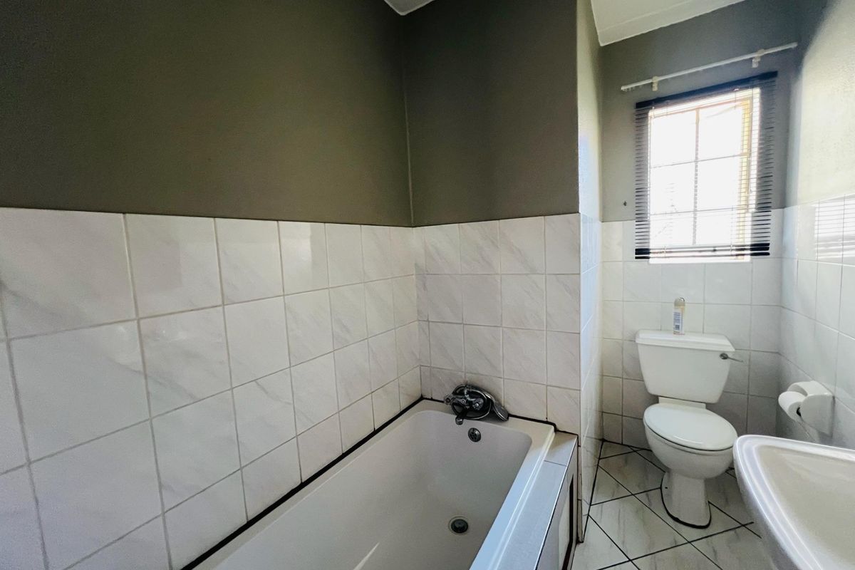 A functional bathroom featuring a bathtub, pedestal basin, and toilet with neutral wall tiling and tiled flooring.