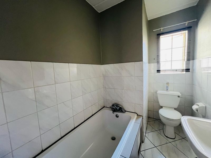 A functional bathroom featuring a bathtub, pedestal basin, and toilet with neutral wall tiling and tiled flooring.