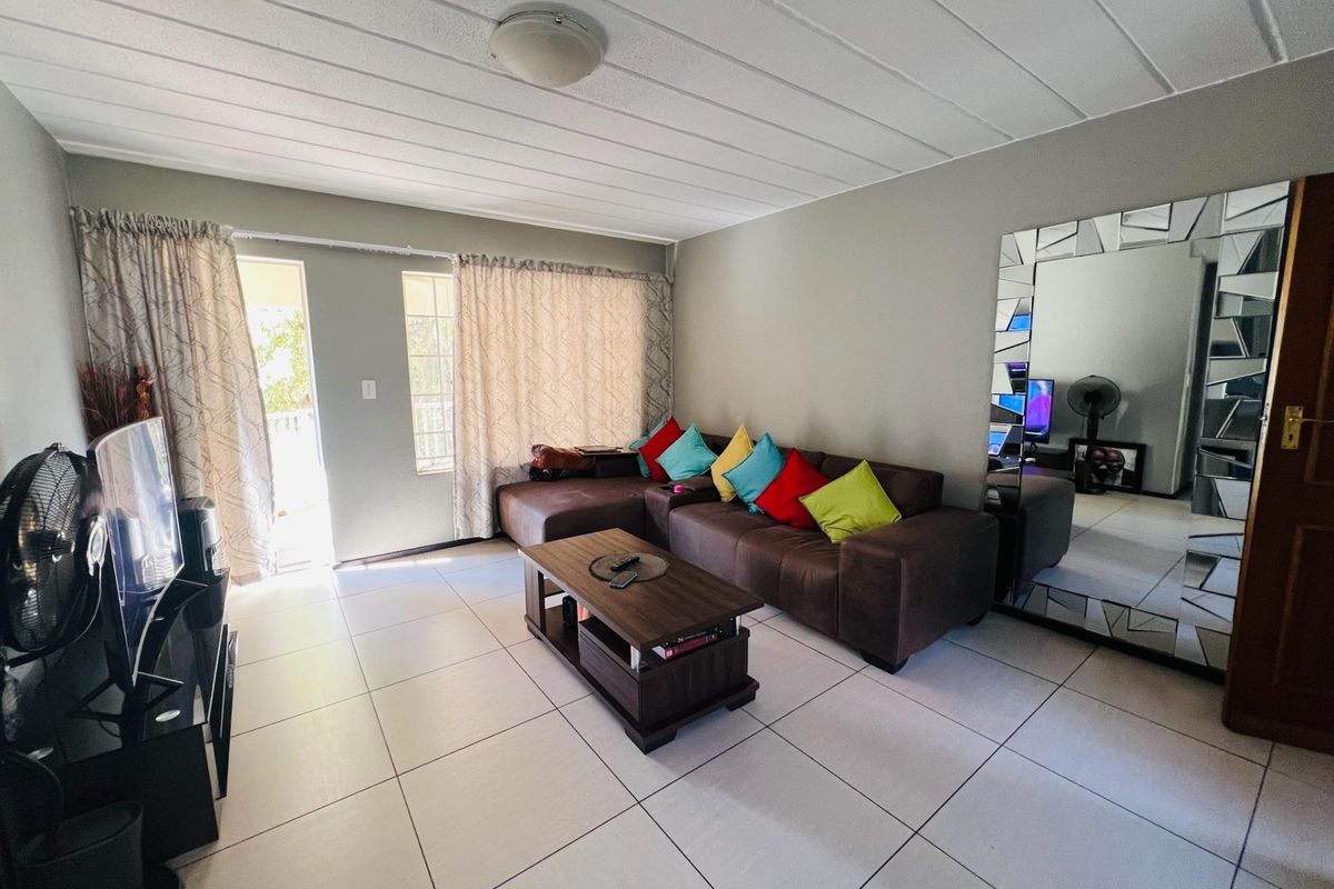 A living room featuring neutral tiled flooring, a ceiling light fixture, and access to an outdoor area through a sliding glass door.