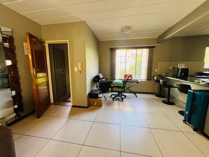Open-plan living area featuring tiled flooring, a breakfast bar, and a security gate, providing a functional and versatile space.