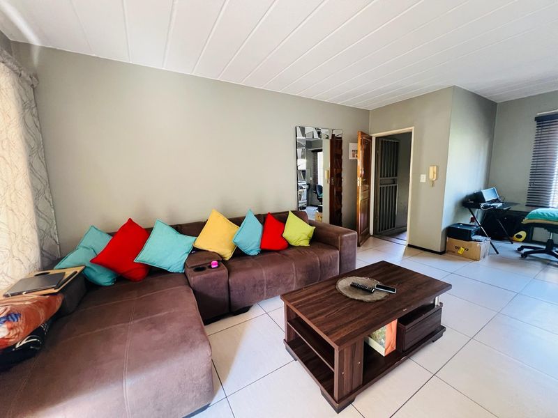 A living room featuring tiled flooring, a panelled ceiling, and an integrated security gate, providing a functional and accessible living space.