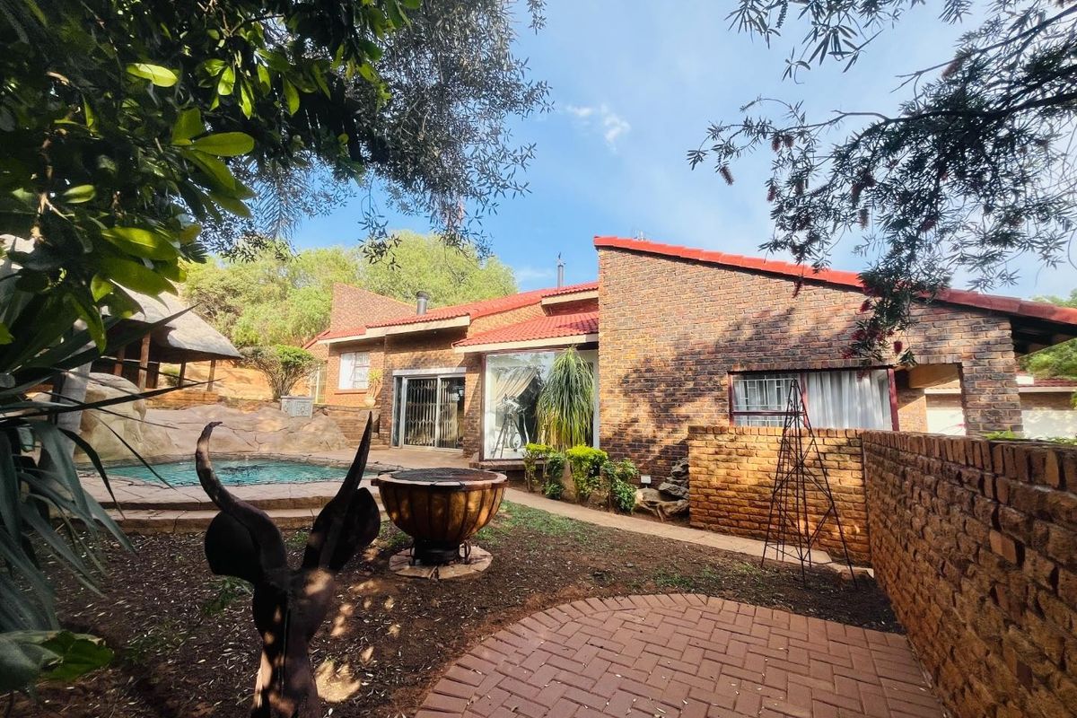 Rear exterior view featuring a brick house with a tiled roof, swimming pool, paved patio area, and established garden surroundings.