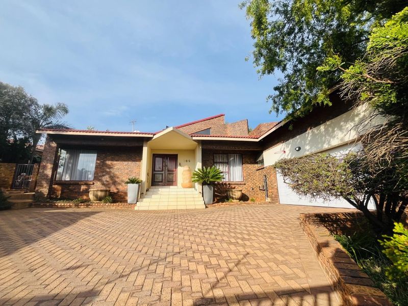 A well-maintained face brick family home featuring a spacious paved driveway, double garage, and a welcoming covered entrance with tiled steps.