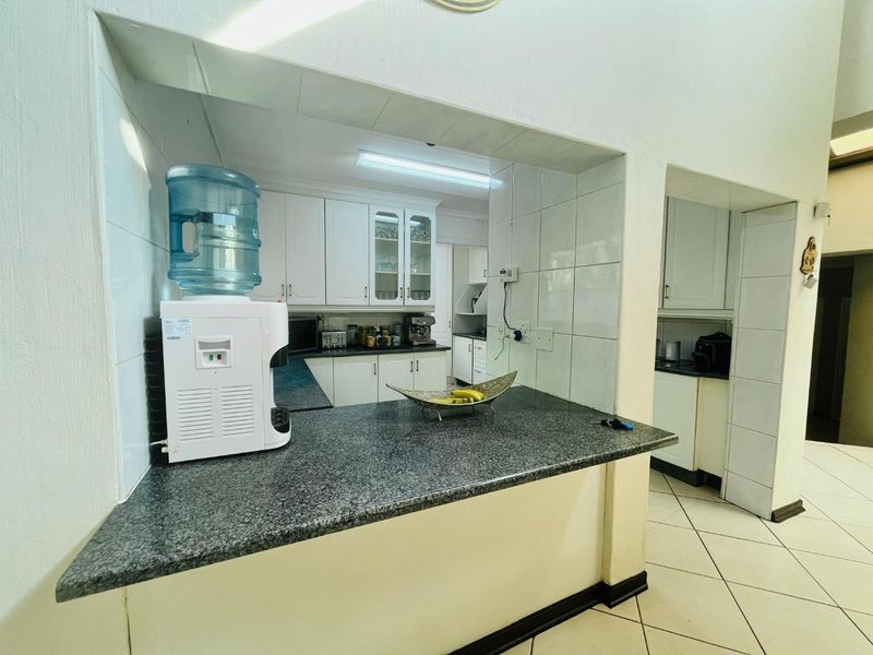 A functional kitchen featuring granite countertops, white cabinetry, and tiled finishes, offering a practical layout with a serving hatch to the adjacent living area.