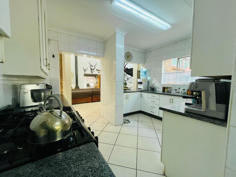 A functional kitchen featuring white cabinetry, granite countertops, a gas hob, and tiled finishes, with an open-plan flow into the adjacent living area.