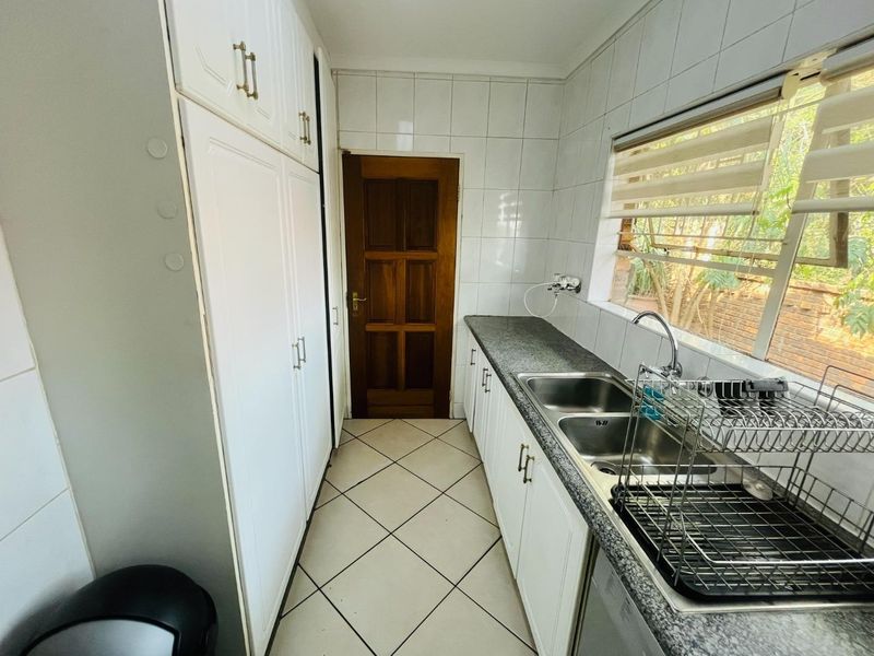 A functional scullery featuring built-in white cabinetry, granite countertops, a double stainless steel sink, and tiled finishes throughout.