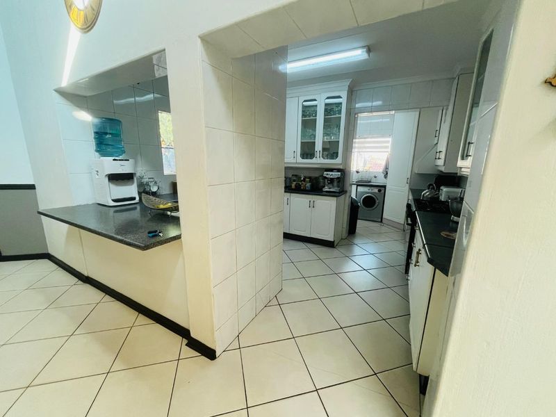 A functional kitchen featuring granite countertops, ample built-in cabinetry, and tiled flooring, with an adjacent scullery area visible through the doorway.