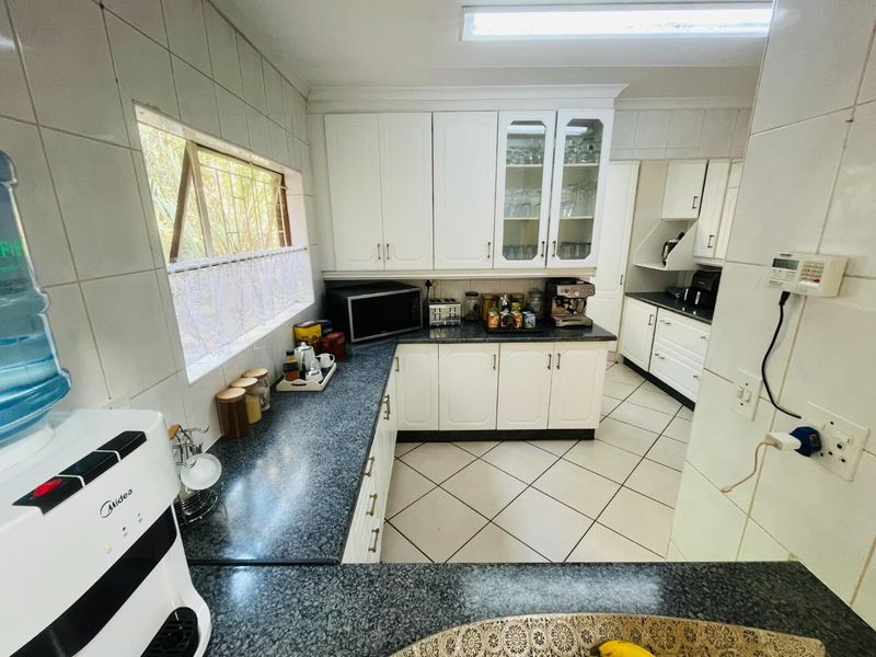 A functional kitchen featuring white built-in cabinetry, dark granite countertops, and tiled flooring, with an adjacent scullery area visible.