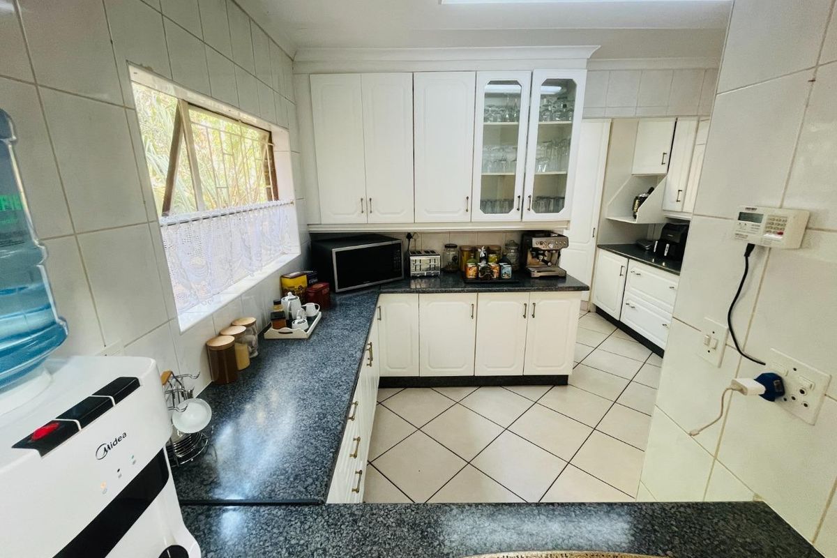A functional kitchen featuring white built-in cabinetry, dark granite countertops, and tiled flooring, with an adjacent scullery area visible.