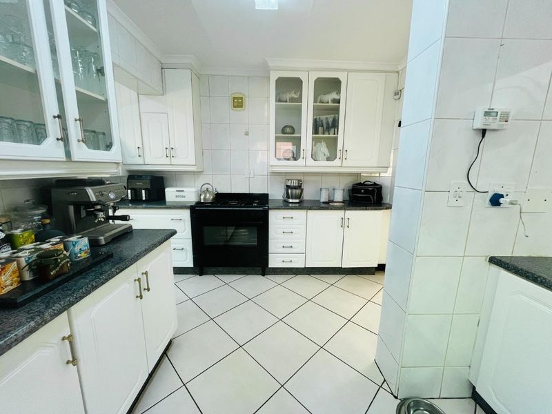 A functional kitchen featuring white cabinetry, granite countertops, a black gas stove, and tiled flooring with a classic backsplash.