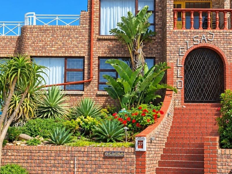 A well-maintained face brick front facade featuring an arched entrance, a balcony, and landscaped terraced gardens.