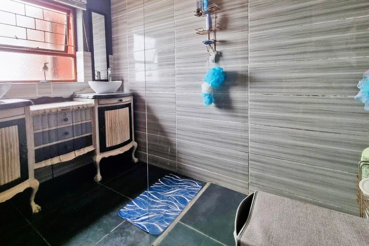 A bathroom featuring a vessel sink on a vanity cabinet, a glass shower screen, and modern horizontal wall tiling.