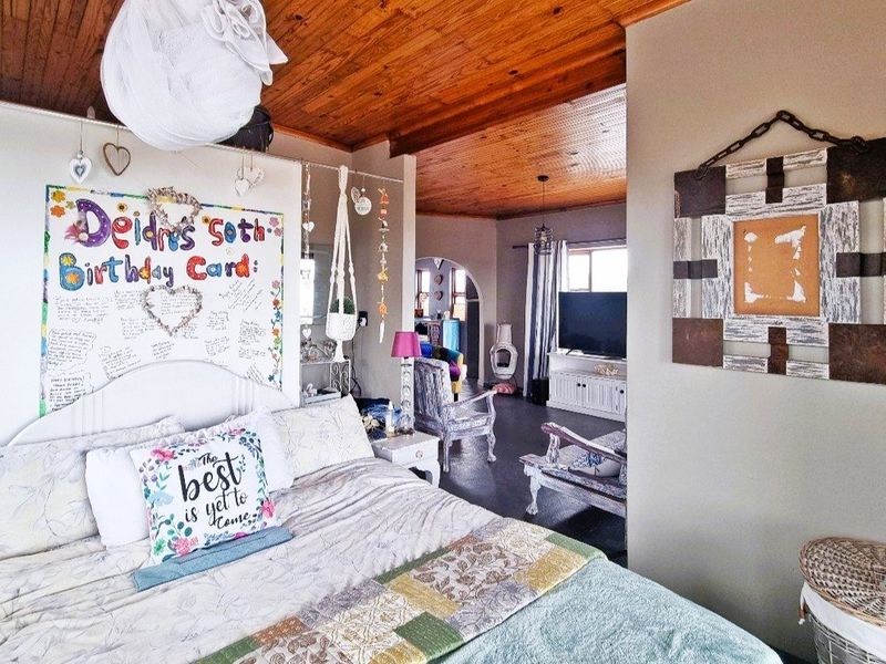 A bedroom featuring a warm timber tongue and groove ceiling, with an open layout leading into an adjacent living area.