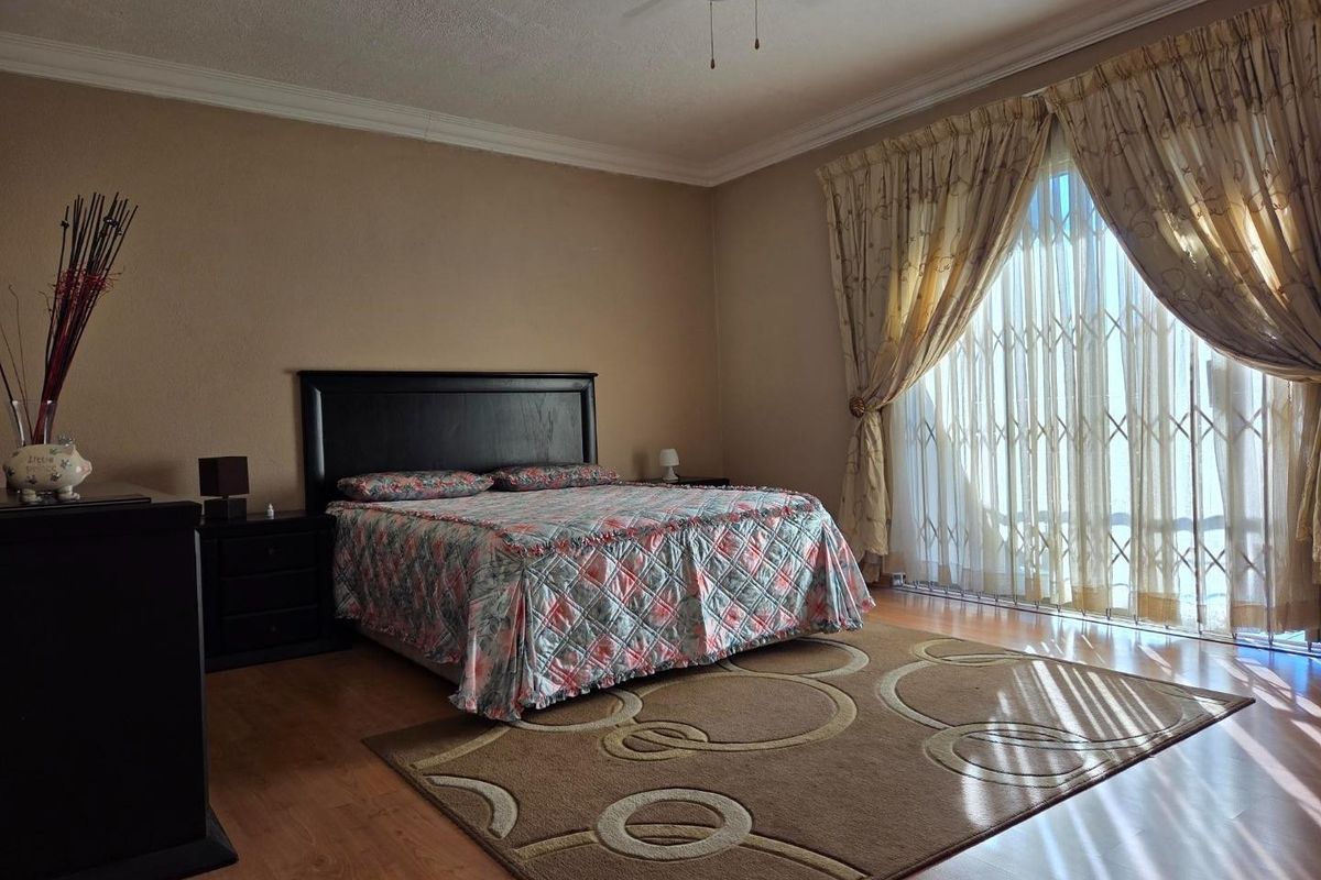 Spacious bedroom featuring laminate flooring, a ceiling fan, and a large sliding glass door with a security gate providing natural light.