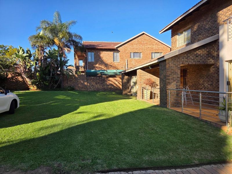 A spacious rear garden featuring a well-maintained lawn, a covered patio with stainless steel balustrades, and a classic face-brick exterior finish.