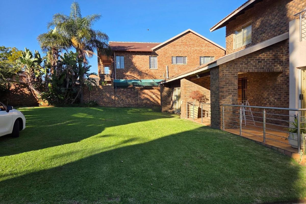 A spacious rear garden featuring a well-maintained lawn, a covered patio with stainless steel balustrades, and a classic face-brick exterior finish.