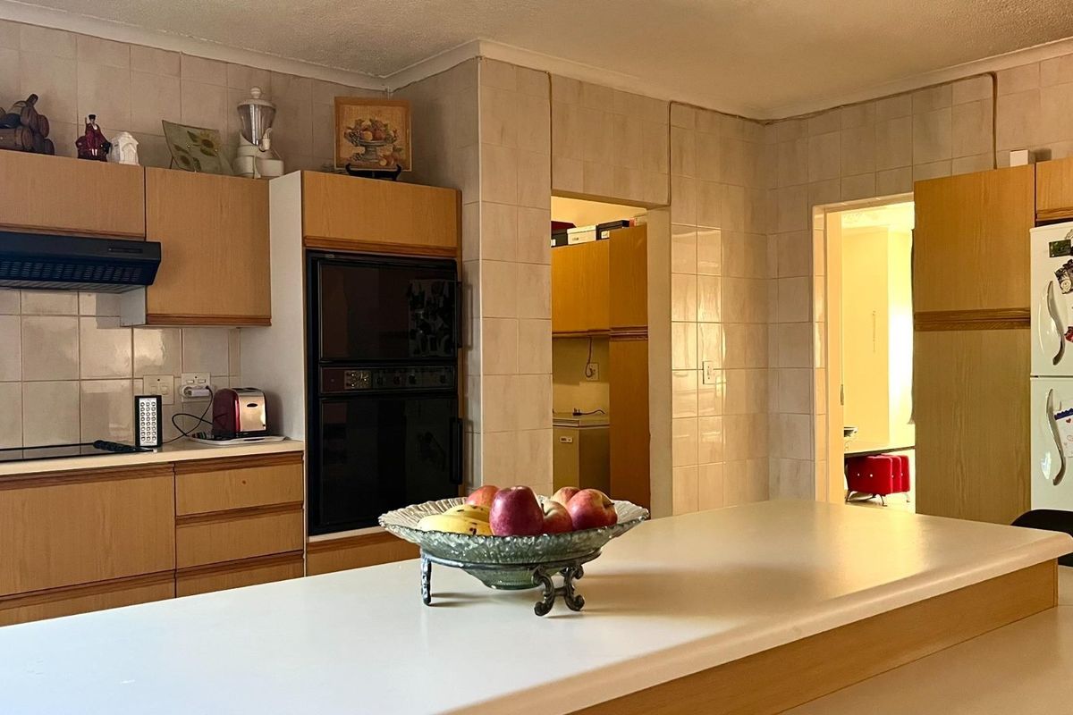 A functional kitchen featuring wood-finish cabinetry, built-in double ovens, an extractor fan, and tiled wall finishes with a central island counter.