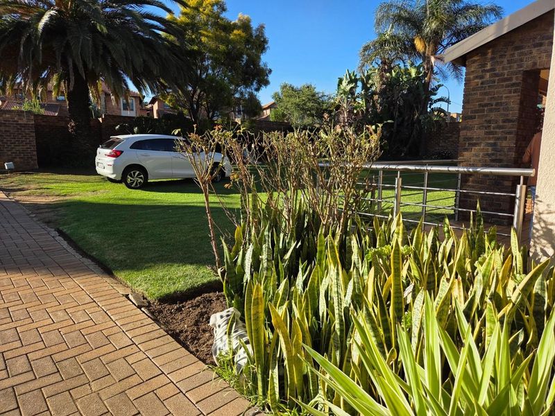 A well-maintained rear garden area featuring brick paving, a manicured lawn, and a modern stainless steel balustrade.