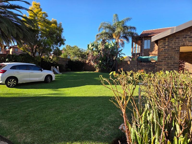 A spacious rear garden featuring a well-maintained lawn, established trees, and brick boundary walls, adjacent to the main house structure.