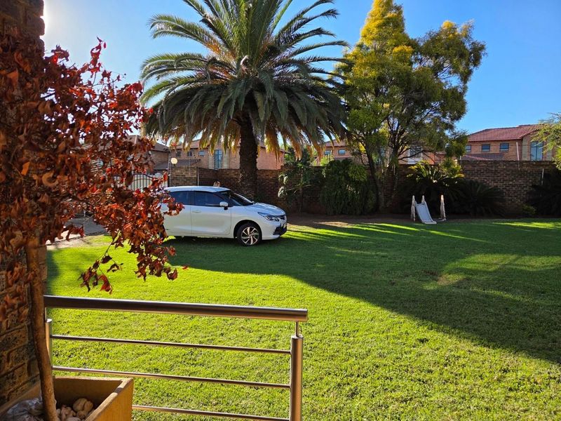 A spacious private garden featuring a well-maintained lawn, mature palm tree, and secure brick boundary walling.