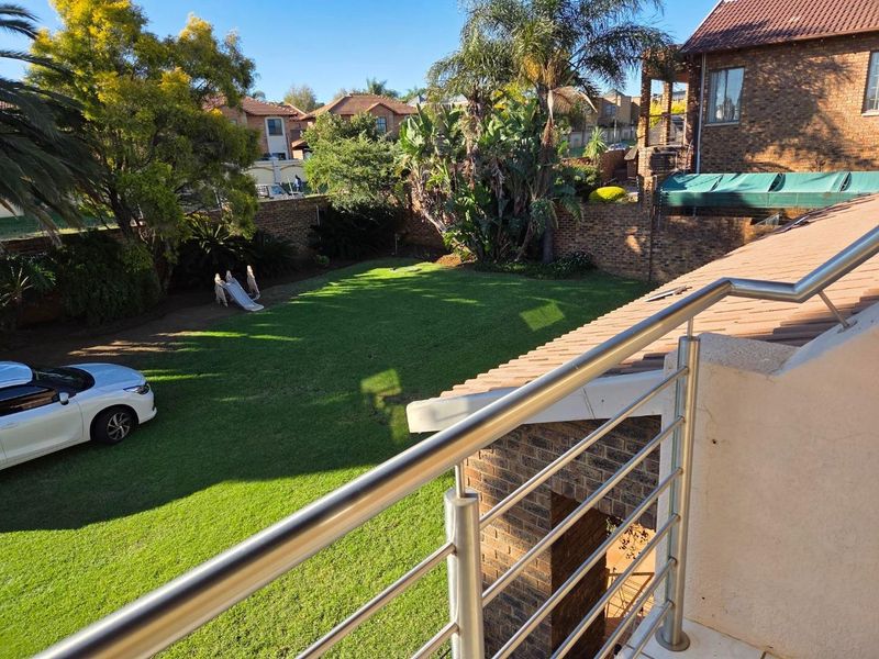 Elevated balcony view overlooking a private garden with a well-maintained lawn and brick boundary wall.