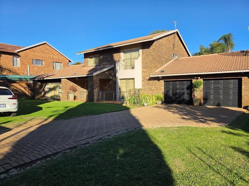 A well-maintained double-story brick house featuring a paved driveway, double garage, and a front balcony with metal railings.