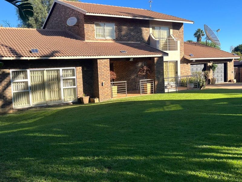 Rear view of a double-story brick house featuring a covered patio, balcony, and a spacious lawn area.