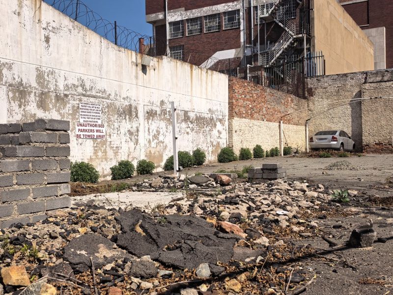 A vacant commercial lot featuring a perimeter wall with razor wire and a degraded asphalt surface requiring site clearance and maintenance.