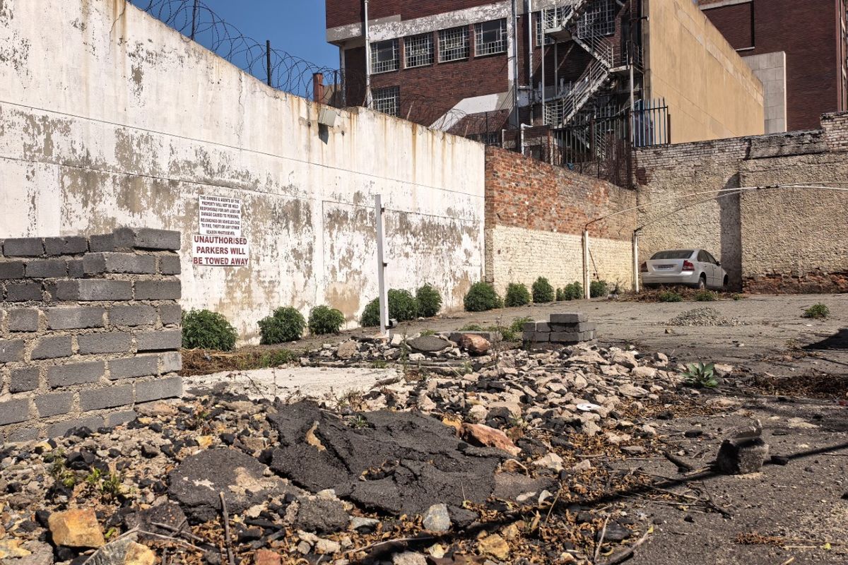A vacant commercial lot featuring a perimeter wall with razor wire and a degraded asphalt surface requiring site clearance and maintenance.
