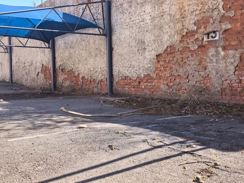 Commercial vacant land featuring an asphalt parking area with a blue shade sail structure and a boundary wall showing significant plaster deterioration.