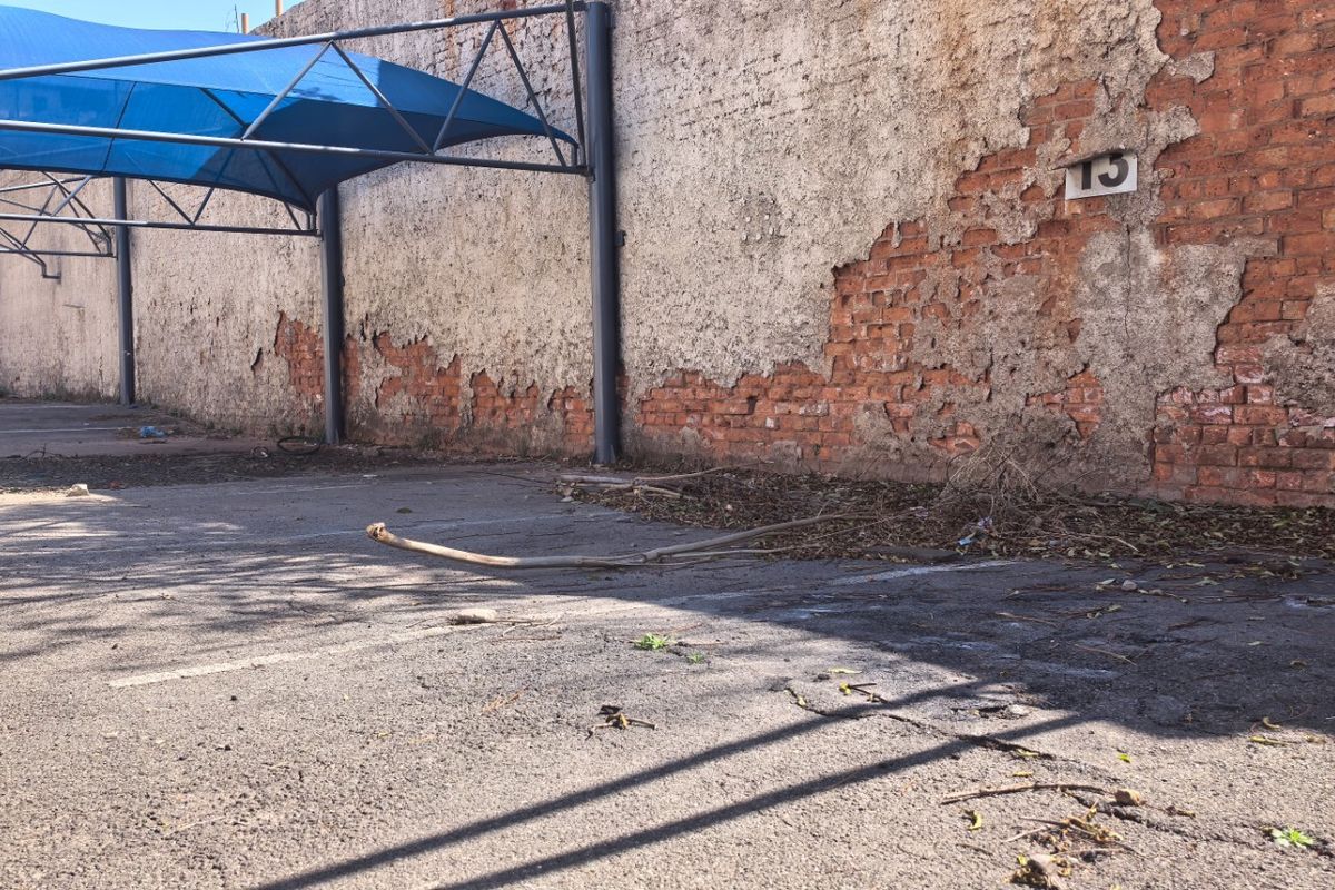 Commercial vacant land featuring an asphalt parking area with a blue shade sail structure and a boundary wall showing significant plaster deterioration.