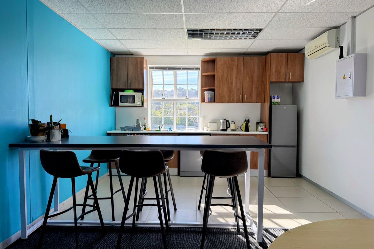A functional office kitchenette featuring wood-finish cabinetry, laminate countertops, a stainless steel sink, and a drop ceiling with integrated lighting.