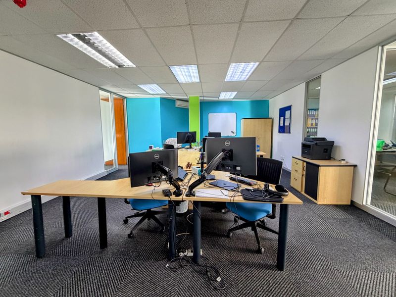 A functional open-plan office space featuring suspended ceilings, recessed lighting, glass partitions, and durable carpet tiles, providing a professional work environment.