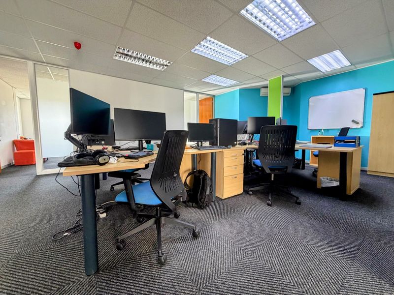 A functional office space featuring carpeted flooring, suspended ceilings with recessed lighting, and glass partitions, providing a professional work environment.