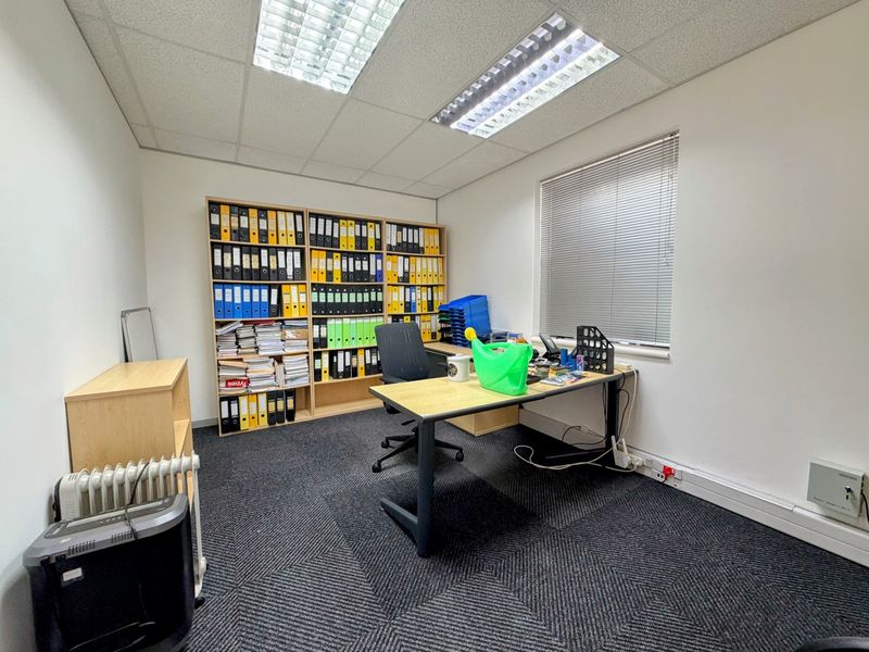 A functional office space featuring carpeted flooring, suspended ceiling with integrated lighting, and window blinds, providing a practical work environment.