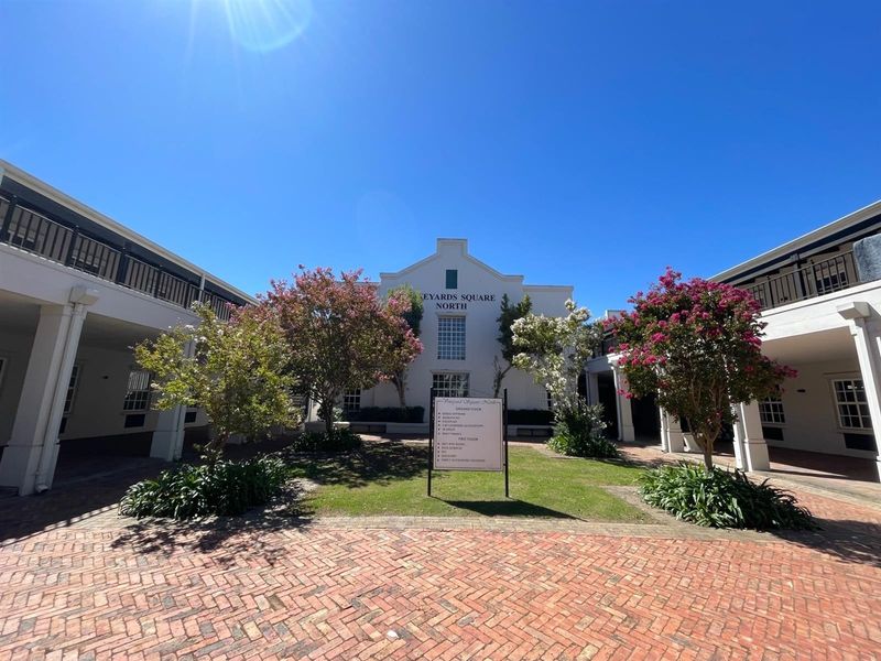 A well-maintained office courtyard featuring brick paving, landscaped gardens, and covered walkways leading to the main building entrance.