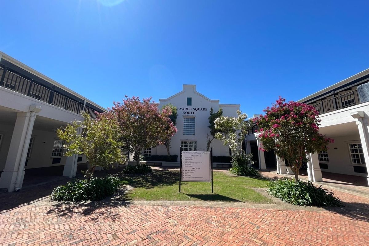A well-maintained office courtyard featuring brick paving, landscaped gardens, and covered walkways leading to the main building entrance.