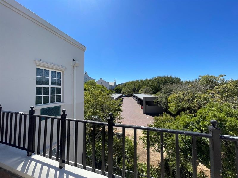 An elevated view overlooking the rear of the office property, featuring a paved driveway, covered parking bays, and mature surrounding trees.