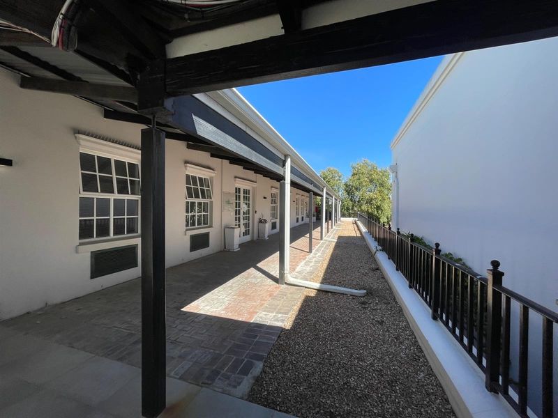 A covered outdoor walkway featuring brick paving, timber support beams, and metal railings, providing access to office units.