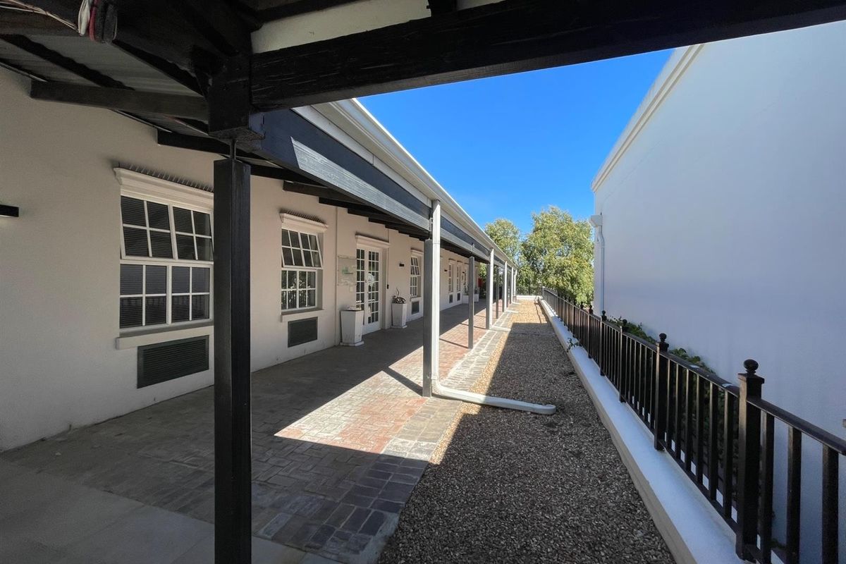 A covered outdoor walkway featuring brick paving, timber support beams, and metal railings, providing access to office units.