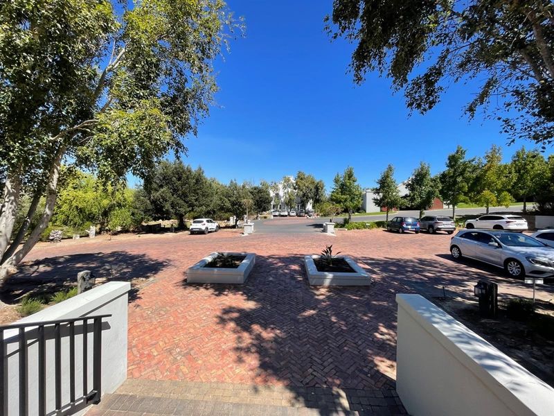 A well-maintained brick paved entrance driveway featuring raised masonry planters and mature trees, leading towards the main office building complex.