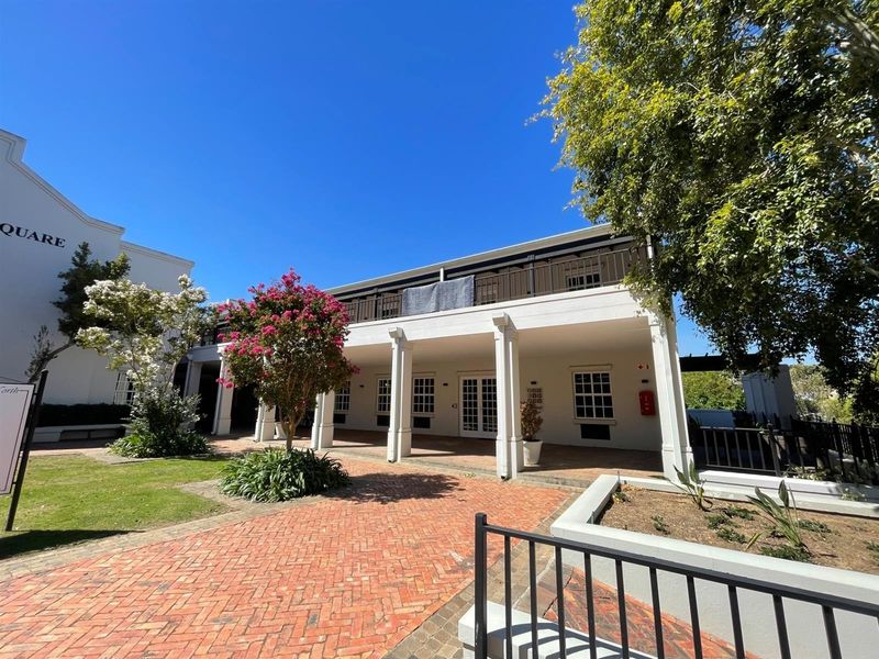 A well-maintained office building exterior featuring a covered ground-floor patio, an upper-level balcony, and a brick-paved courtyard area.