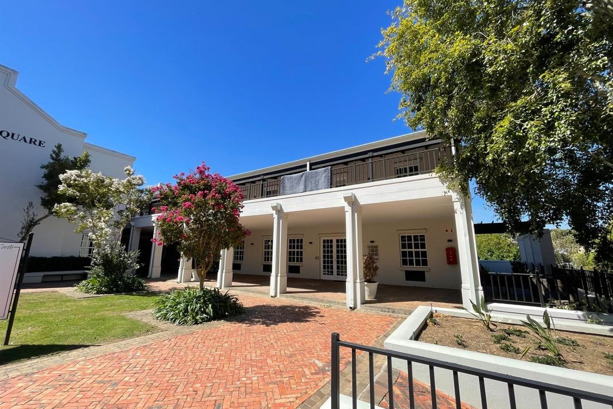 A well-maintained office building exterior featuring a covered ground-floor patio, an upper-level balcony, and a brick-paved courtyard area.