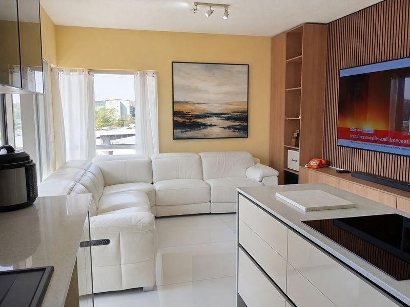 Modern open-plan living area featuring a sleek kitchen island with induction hob, tiled floors, and a feature wall with built-in shelving.