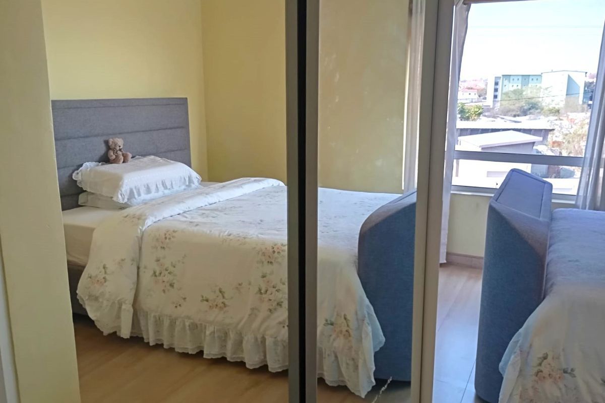 A bedroom featuring laminate flooring and a built-in mirrored wardrobe, offering natural light and a view through the window.