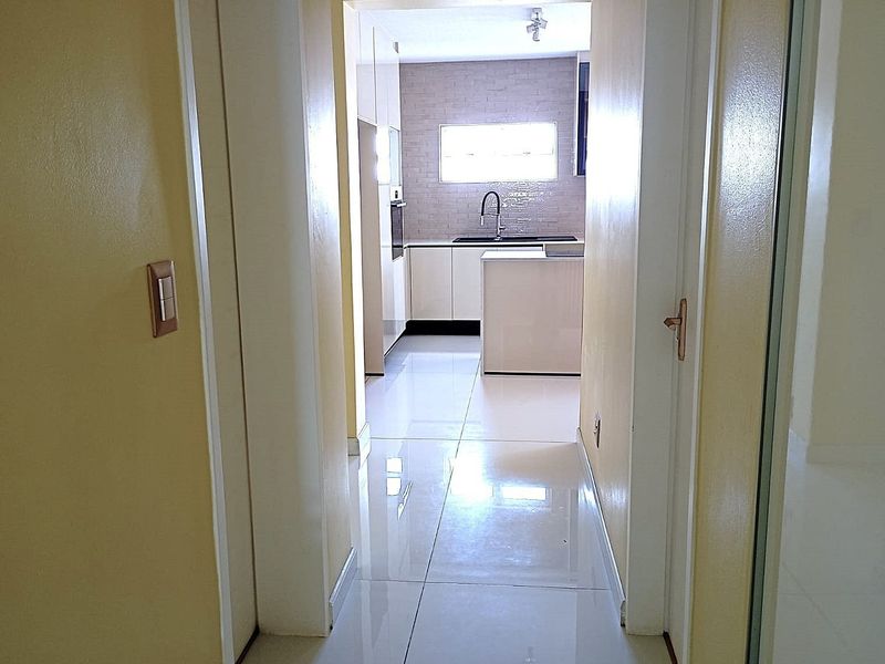 A bright hallway leading into a modern, open-plan kitchen featuring tiled floors, sleek cabinetry, and a central island.