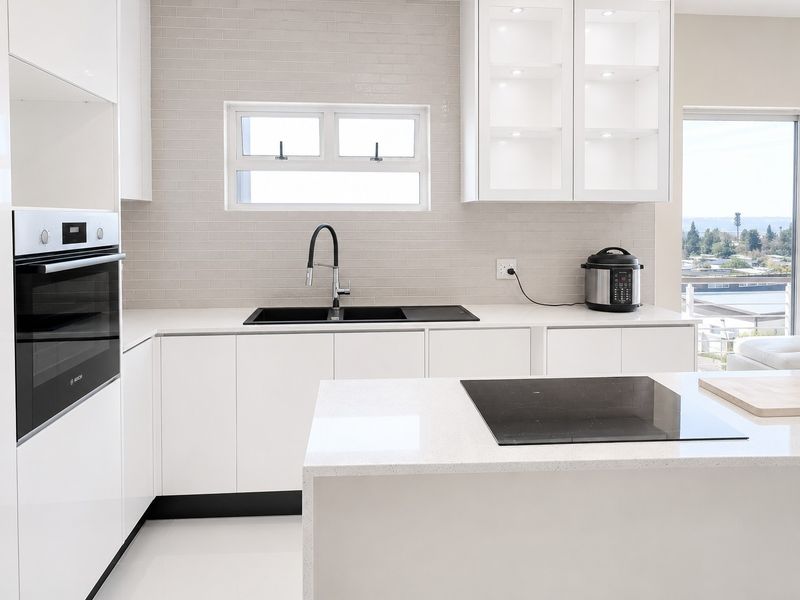 Modern kitchen featuring sleek white cabinetry, quartz countertops, subway tile backsplash, built-in oven, induction hob, and high-quality finishes with ample natural light.
